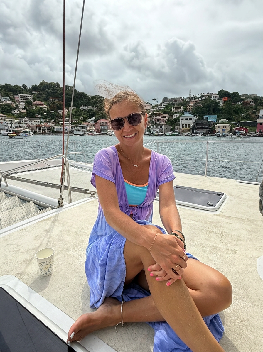 Hannah sitting on the deck of a sailboat, smiling, with a harbor town behind her