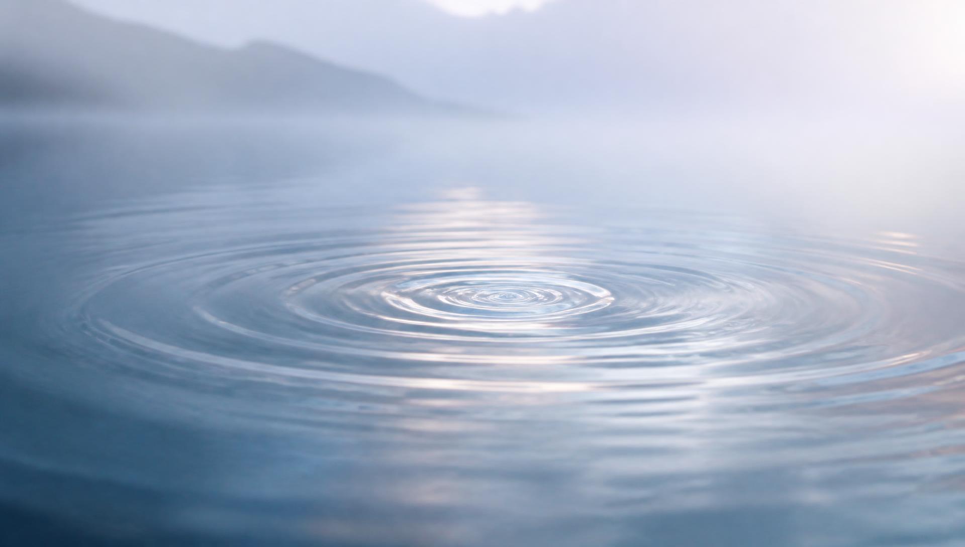 Still water with gentle ripples spreading across a misty surface